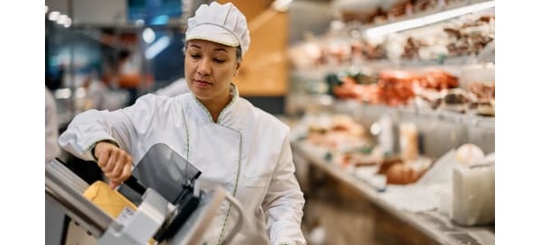 Supermarket worker using a slicer at delicatessen section.