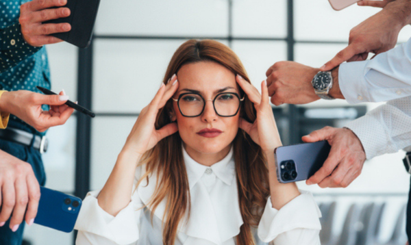 Woman sitting at a desk with her hands pressed to her temples, suggesting stress or overwhelm.