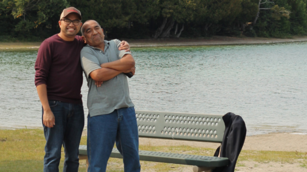 Image of two men standing by a bench and water