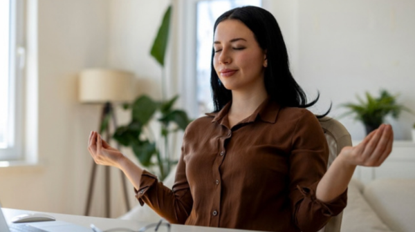 Young businesswoman meditating at her desk during a work break beside her laptop.